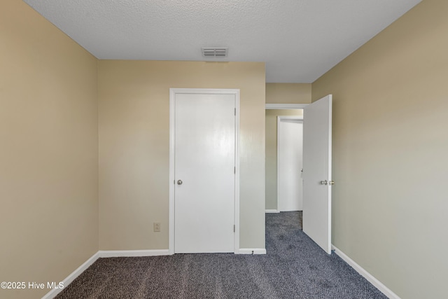 unfurnished bedroom with a textured ceiling and dark colored carpet