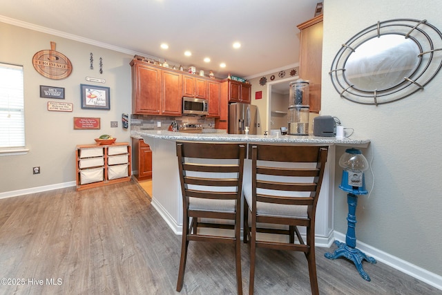 kitchen with a kitchen breakfast bar, wood-type flooring, kitchen peninsula, and appliances with stainless steel finishes