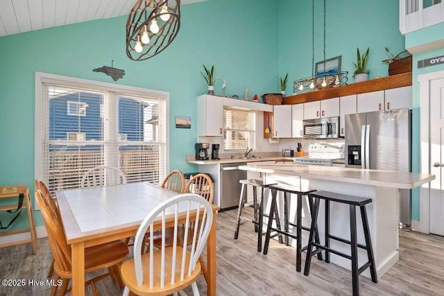 dining room with sink, high vaulted ceiling, and light wood-type flooring