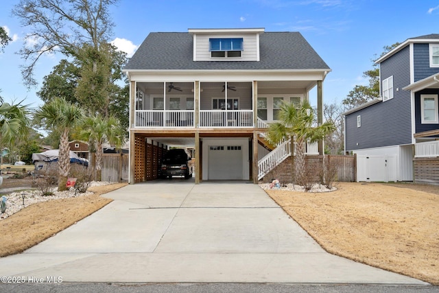 raised beach house with a carport, driveway, an attached garage, stairway, and ceiling fan