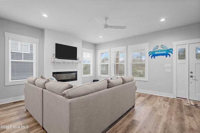 living room with a healthy amount of sunlight, light wood finished floors, a large fireplace, and ceiling fan