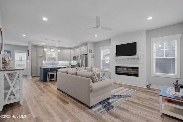 living area with a fireplace, light wood-type flooring, a ceiling fan, and baseboards