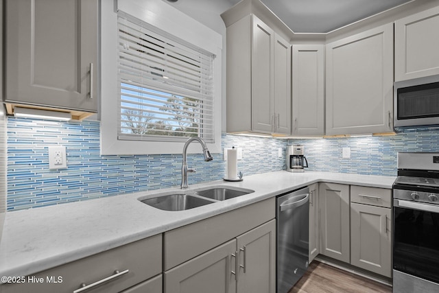 kitchen with a sink, light wood-type flooring, decorative backsplash, gray cabinetry, and appliances with stainless steel finishes