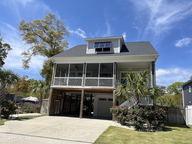 raised beach house with stairway, driveway, a shingled roof, fence, and ceiling fan