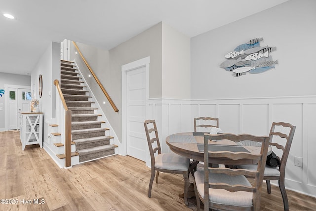 dining space with stairway, a decorative wall, a wainscoted wall, and wood finished floors