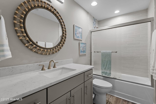 bathroom with toilet, recessed lighting, wood finished floors, combined bath / shower with glass door, and vanity