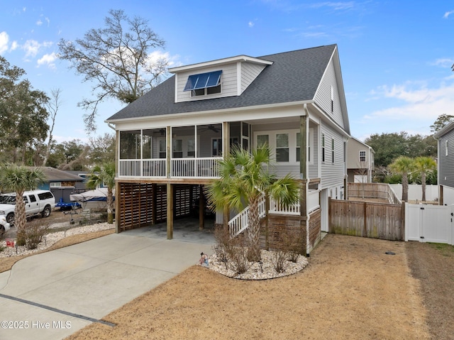 coastal inspired home with concrete driveway, fence, a ceiling fan, a shingled roof, and a sunroom