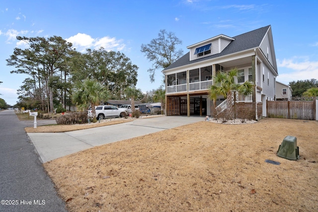 view of front of property featuring a ceiling fan, fence, a shingled roof, driveway, and a sunroom
