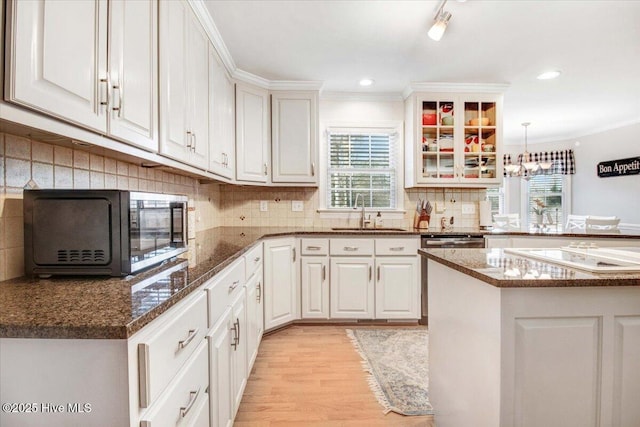 kitchen with white cabinets, dark stone counters, ornamental molding, light hardwood / wood-style flooring, and sink