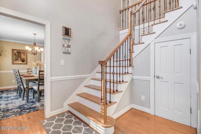 stairway featuring a notable chandelier, ornamental molding, and hardwood / wood-style flooring