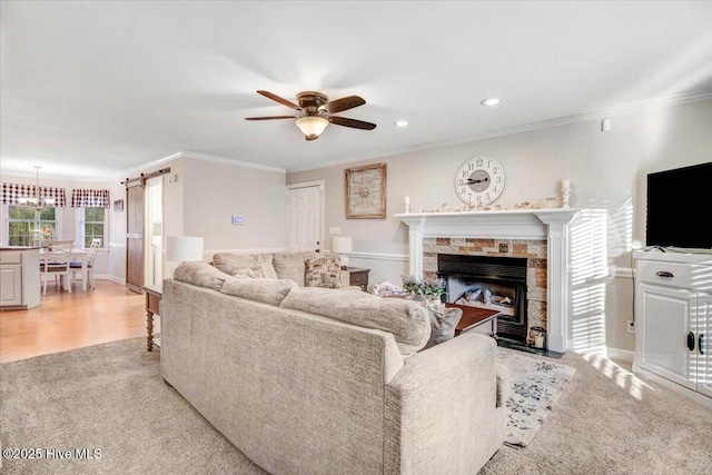 carpeted living room featuring ceiling fan with notable chandelier, crown molding, and a fireplace