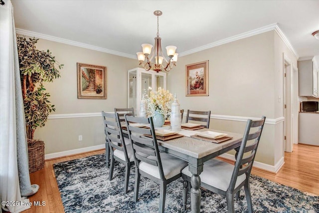 dining room featuring crown molding, light wood-type flooring, and an inviting chandelier