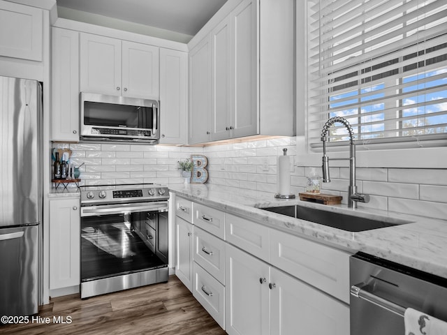 kitchen featuring light stone countertops, appliances with stainless steel finishes, white cabinets, and sink