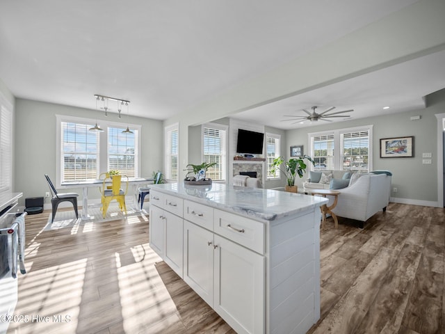 kitchen featuring light stone countertops, white cabinetry, a stone fireplace, light wood-type flooring, and ceiling fan