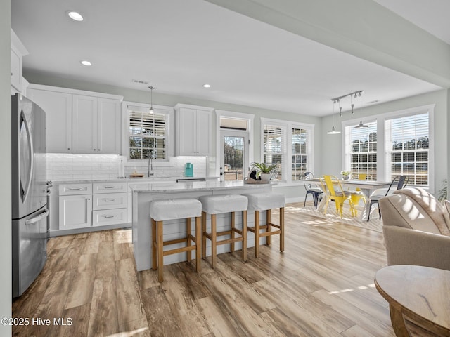 kitchen featuring a center island, hanging light fixtures, white cabinets, stainless steel fridge, and light stone counters