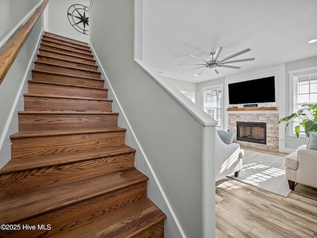 stairway featuring ceiling fan, a stone fireplace, and hardwood / wood-style floors