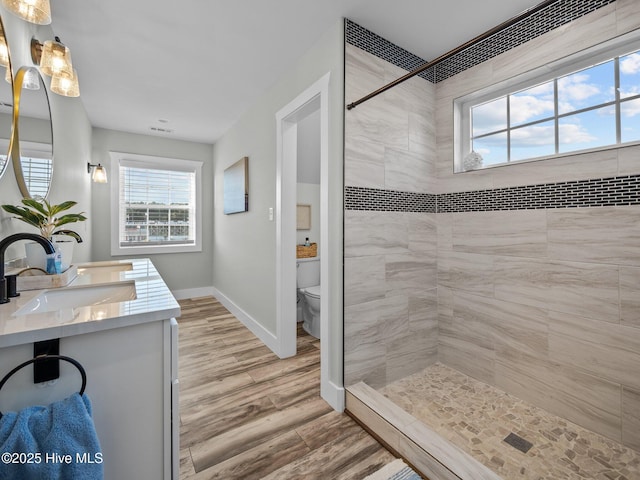 bathroom with toilet, tiled shower, wood-type flooring, and vanity