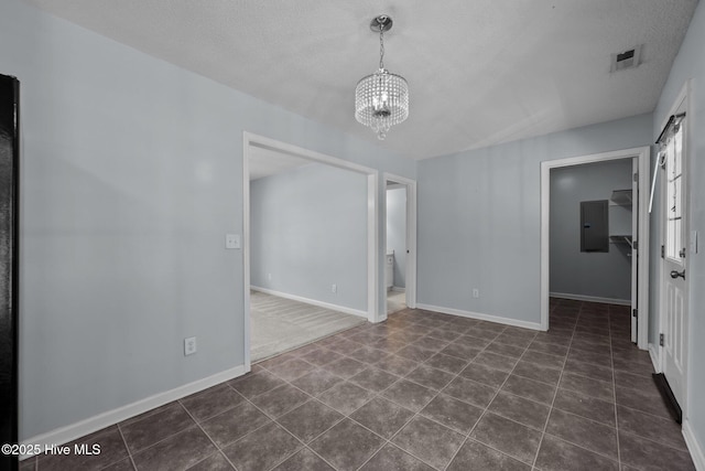 empty room with electric panel, a textured ceiling, dark tile patterned flooring, and a notable chandelier