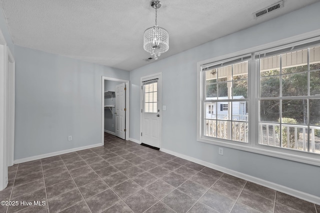 tiled empty room with a notable chandelier and a textured ceiling