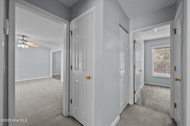 hallway featuring light colored carpet and a textured ceiling