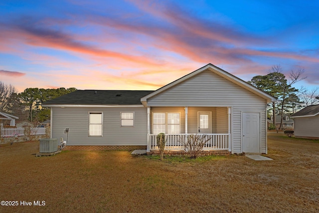 back house at dusk featuring a yard, central AC unit, and covered porch