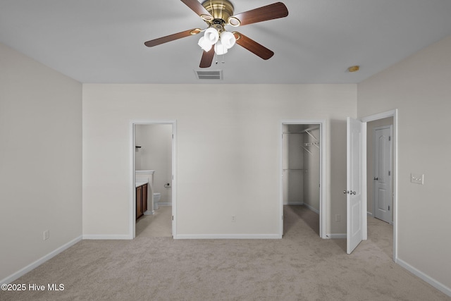 unfurnished bedroom featuring ensuite bath, a walk in closet, light carpet, a closet, and ceiling fan