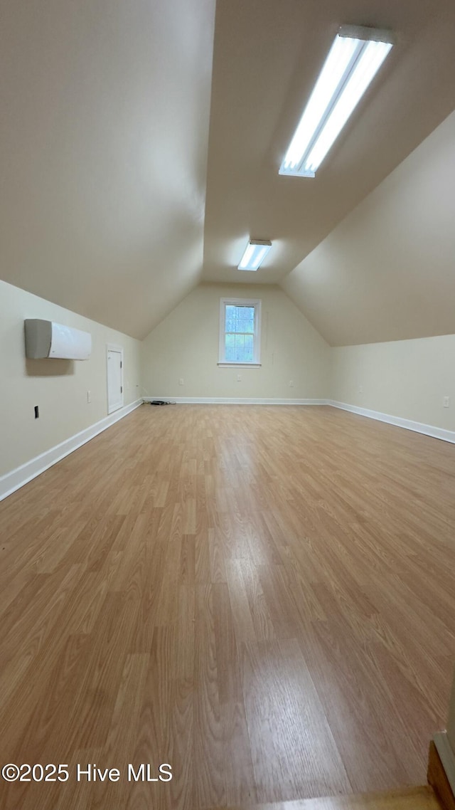 additional living space featuring light wood-type flooring and vaulted ceiling with skylight