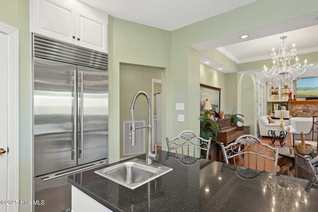 kitchen with decorative light fixtures, sink, ornamental molding, white cabinets, and built in fridge