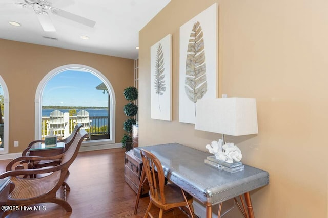 office space with ceiling fan, a water view, and wood-type flooring