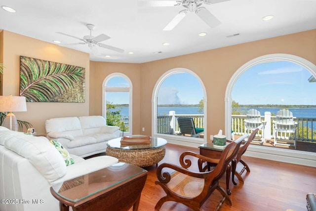 living room with ceiling fan, a water view, and wood-type flooring