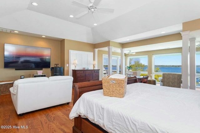 bedroom with lofted ceiling, wood-type flooring, a raised ceiling, a water view, and ceiling fan