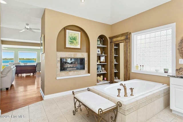 bathroom featuring ceiling fan, vanity, tile patterned floors, built in shelves, and a relaxing tiled tub