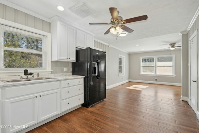 kitchen featuring ceiling fan, black fridge, sink, white cabinetry, and ornamental molding