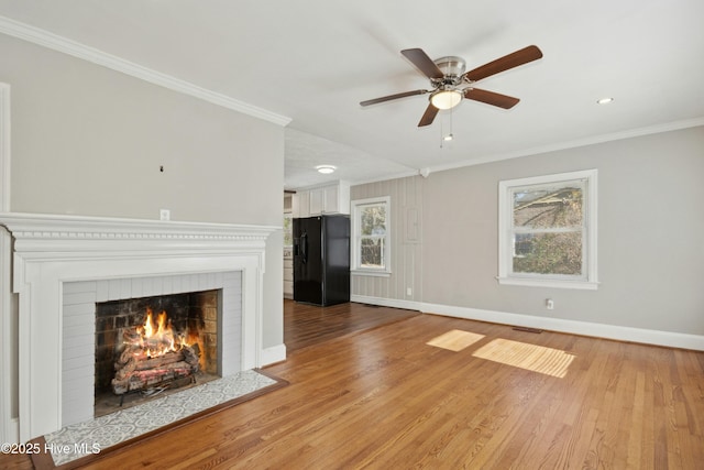 unfurnished living room featuring a brick fireplace, ornamental molding, light hardwood / wood-style floors, and ceiling fan