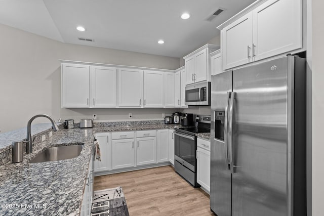 kitchen with appliances with stainless steel finishes, white cabinets, light wood-type flooring, sink, and dark stone counters