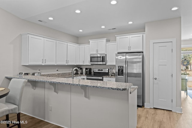 kitchen with kitchen peninsula, white cabinets, light wood-type flooring, a kitchen bar, and stainless steel appliances