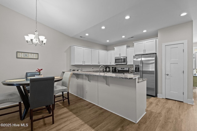 kitchen with appliances with stainless steel finishes, white cabinets, decorative light fixtures, kitchen peninsula, and a breakfast bar area