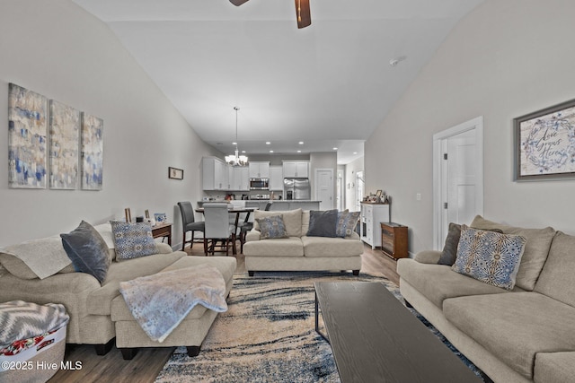 living room featuring ceiling fan with notable chandelier, wood-type flooring, and vaulted ceiling