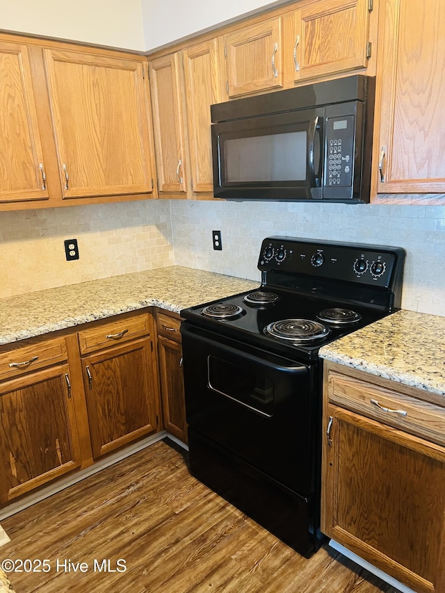 kitchen featuring dark hardwood / wood-style floors, decorative backsplash, light stone counters, and black appliances