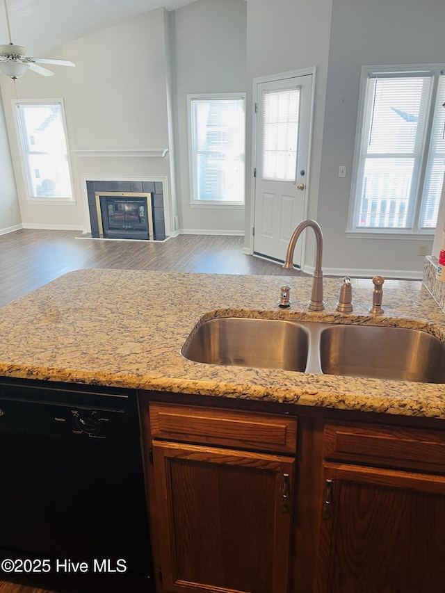 kitchen with sink, light hardwood / wood-style flooring, a tile fireplace, black dishwasher, and light stone countertops