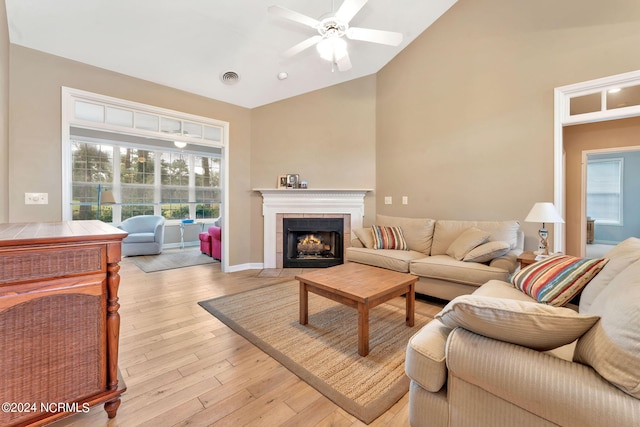 living room with ceiling fan, lofted ceiling, a tiled fireplace, and light wood-type flooring