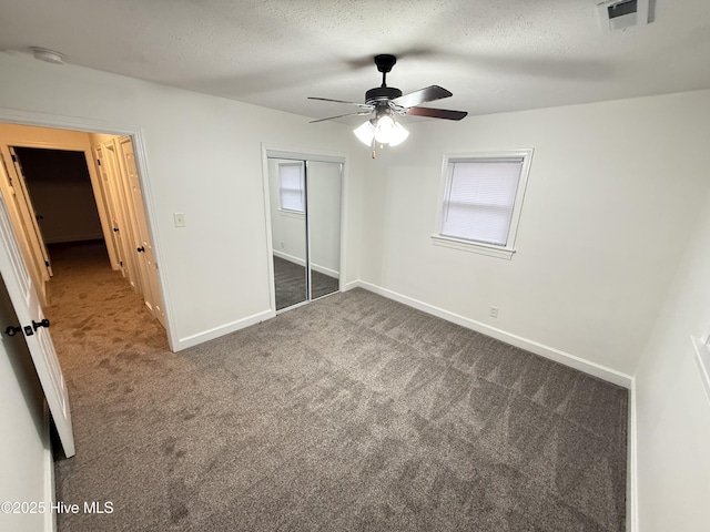 unfurnished bedroom featuring a textured ceiling, ceiling fan, a closet, and dark carpet