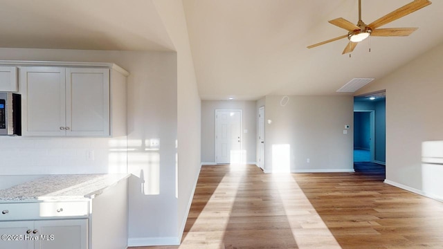 kitchen with ceiling fan, lofted ceiling, white cabinets, light stone countertops, and light hardwood / wood-style flooring