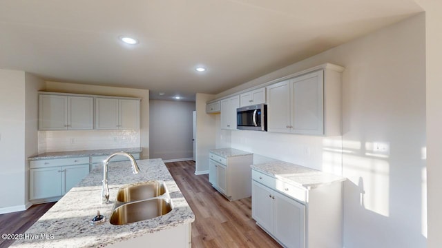 kitchen with light hardwood / wood-style floors, sink, white cabinets, and a kitchen island with sink