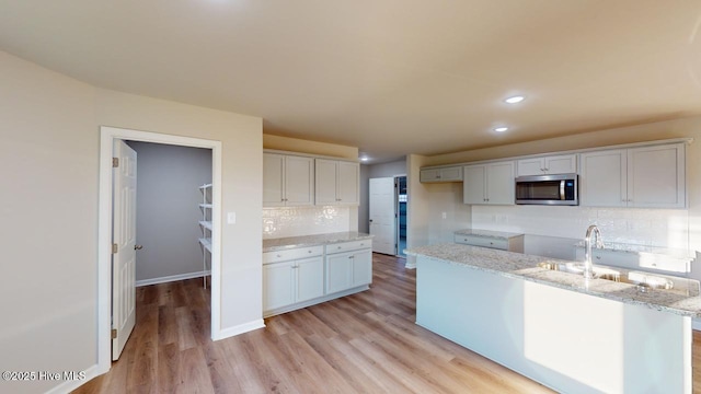 kitchen with tasteful backsplash, light hardwood / wood-style floors, sink, white cabinetry, and light stone counters