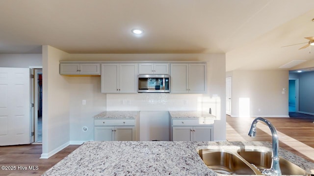 kitchen with ceiling fan, backsplash, wood-type flooring, light stone countertops, and sink