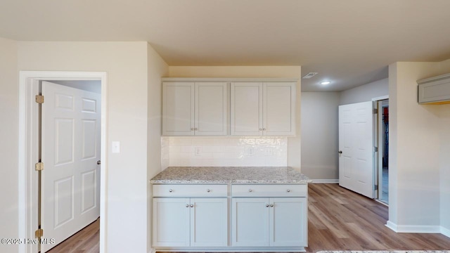 kitchen with tasteful backsplash, light stone countertops, white cabinetry, and light hardwood / wood-style flooring