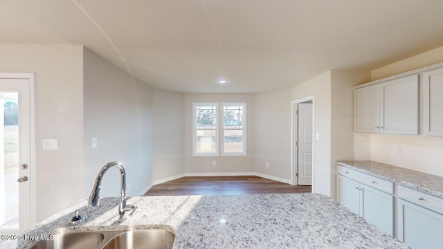 kitchen featuring decorative backsplash, sink, white cabinetry, dark wood-type flooring, and light stone countertops