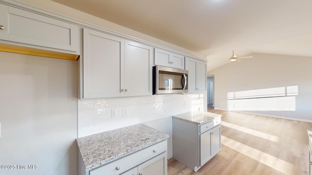 kitchen with light hardwood / wood-style floors, ceiling fan, backsplash, light stone countertops, and vaulted ceiling