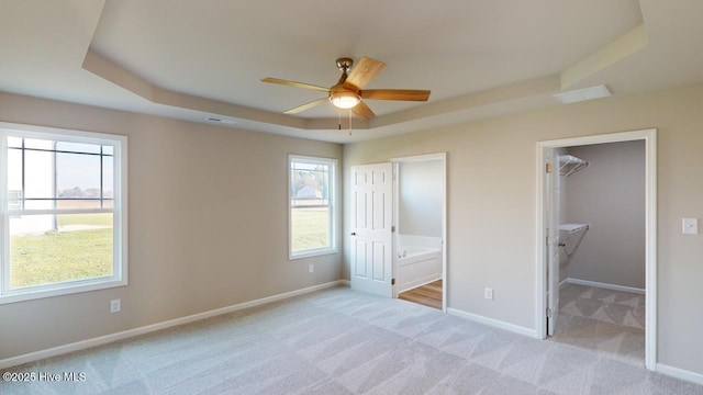 unfurnished bedroom with ensuite bathroom, ceiling fan, a tray ceiling, a closet, and a walk in closet